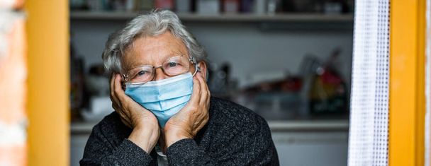 Großaufnahme einer alten Seniorin, die aus dem Fenster schaut, während Covid-19 oder Coronavirus-Pandemie, Quarantäne zu Hause - Foto, Bild