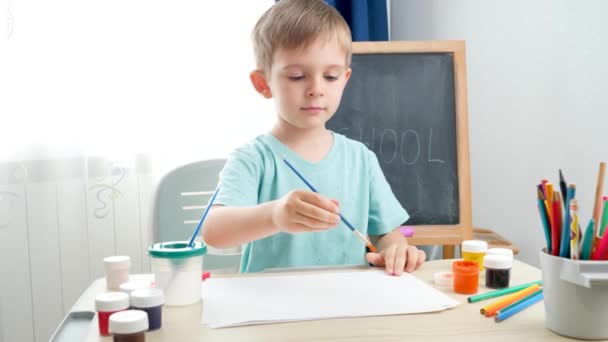 Kleiner Junge zeichnet ein Bild mit Guachefarbe. Kindererziehung zu Hause während der Isolation und Aussperrung. Konzept der Kunst und Kreativität von Kindern - Filmmaterial, Video