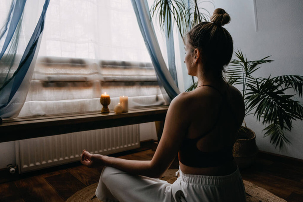 Self-care, self-compassion, mental wellbeing in post-pandemic world. Mental health, wellbeing, meditation to eliminate anxiety. Young woman sitting on floor do yoga exercise and meditation at home - Photo, Image