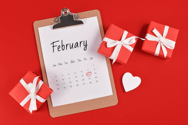 February calendar sheet with Valentine's Day on the 14th marked with red heart surrounded by gift boxes and heart on red background - Photo, Image