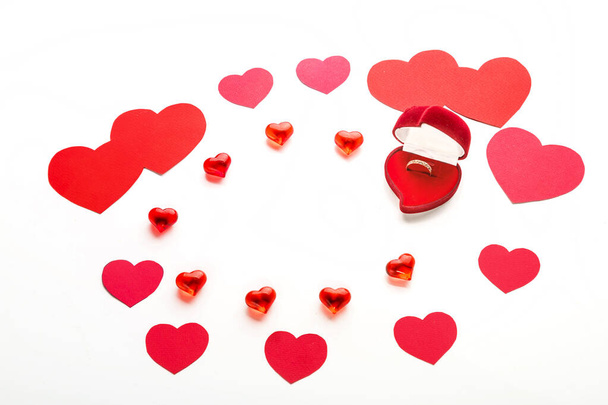 Corazones rojos de diferentes tamaños para el día de San Valentín y corazones de vidrio y una caja en forma de corazón de terciopelo con un anillo sobre un fondo blanco. Fotografía horizontal - Foto, Imagen