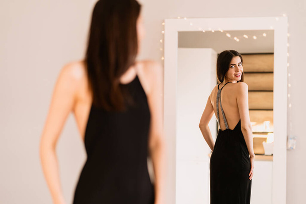 Lady draagt mooie zwarte jurk kijken in de spiegel - Foto, afbeelding