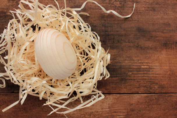 Чистое деревянное пасхальное яйцо для покраски или декупажа в гнезде на деревянном фоне. Вид сверху - Фото, изображение