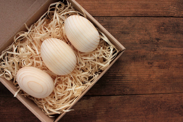 Puste drewniane jaja do malowania lub decoupage w pudełku z prezentami. Pisanki w koszyku na drewnianym stole. Widok z góry - Zdjęcie, obraz