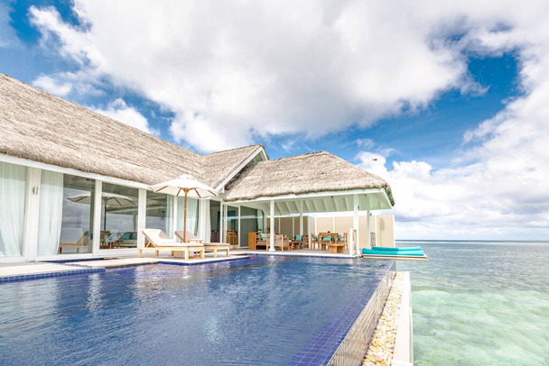 Beautiful infinity poolside with luxury over water villa, luxury travel summer vacation, chaise lounge concept. Luxurious tropical beach landscape, deck chairs and loungers and water reflection. Peaceful, relaxing resort hotel with sea view. - Photo, Image
