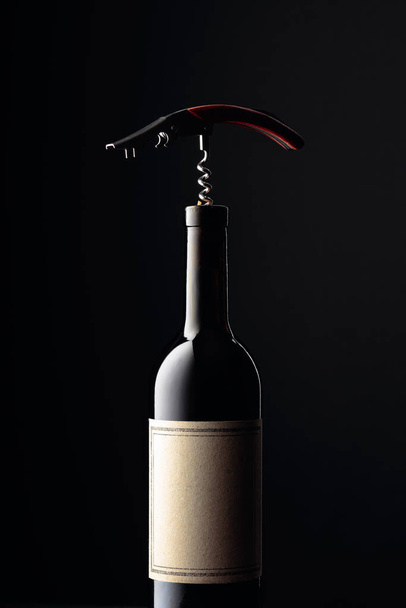 Fles rode wijn met kurkentrekker op een zwarte ondergrond. Kopieerruimte. - Foto, afbeelding