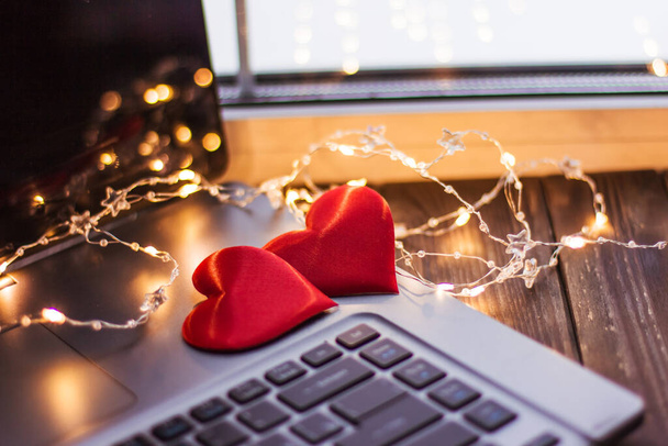 Two red hearts lie on a wooden table near a laptop, Valentine's day wedding love - Foto, imagen