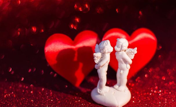 Two little angels with two red hearts on a red background with bokeh, wedding on Valentine's Day - Photo, Image