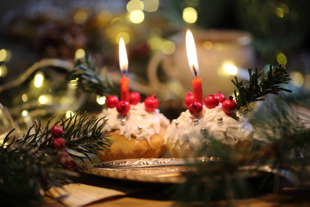 Christmas cupcakes in white glaze with a burning candle on the background of a garland - Foto, immagini