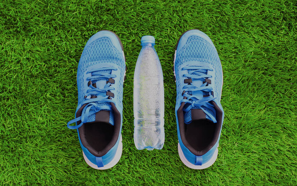 Sports sneakers and plastic bottle of water on a green grass background, blank copy space - Фото, зображення