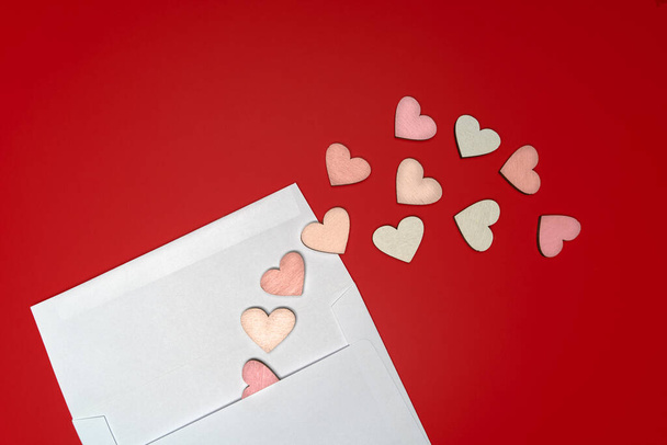 Creative flat lay of paper envelope with hearts around on bright red background. Love concept - Фото, изображение