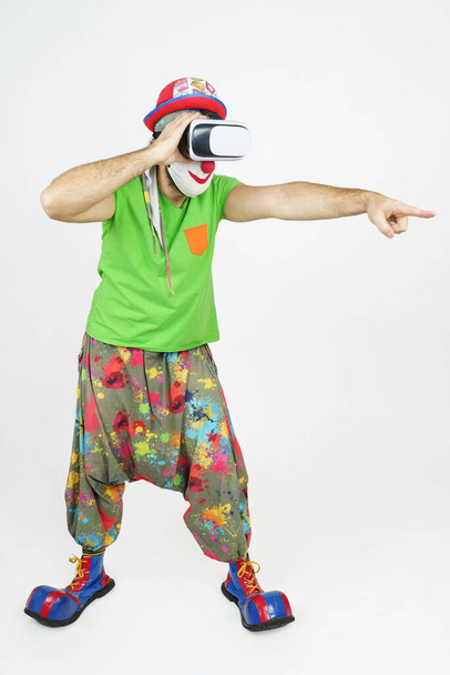 Holiday and fun concept. The clown is playing, he has virtual glasses on his head, he looks like through binoculars - he points his hand forward. Isolated on white - Foto, Imagem