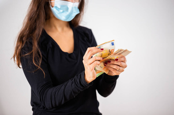 Woman holding money in her hands with face mask covering her mouth and nose - Photo, Image