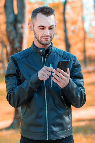 Handsome Guy Using Smartphone at Autumn Park - Foto, afbeelding