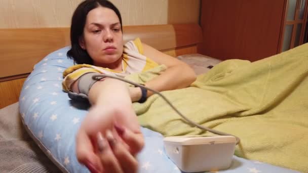 Menina em casa na cama mede a pressão com um tonômetro - Filmagem, Vídeo