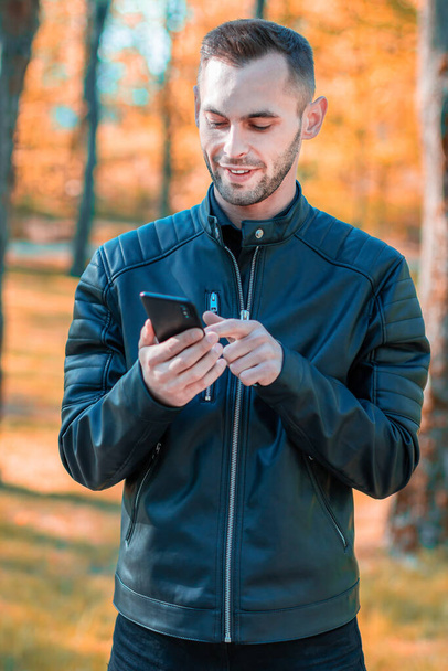 Handsome Guy Using Smartphone at Autumn Park - Foto, imagen