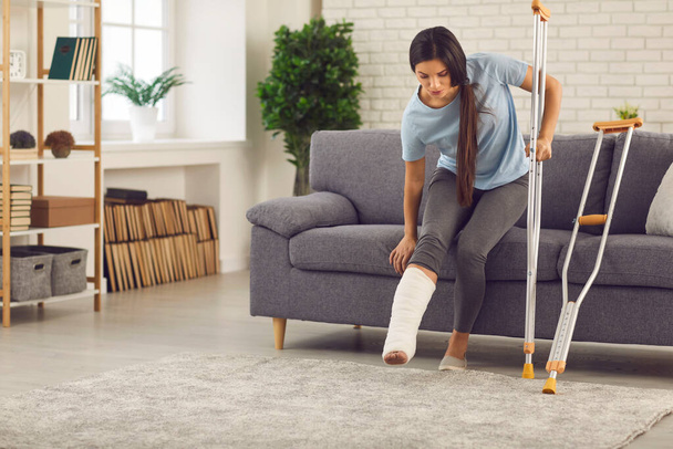 Woman with broken leg trying to stand up and walk with crutches in the living-room - Fotoğraf, Görsel