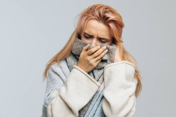 Upset young Caucasian woman with strawberry blonde hair wrapped in warm scarf, feels bad, looking at camera, closeup.Sick desperate female has flu. Rhinitis, cold, sickness, allergy concept.Flu season - Photo, Image