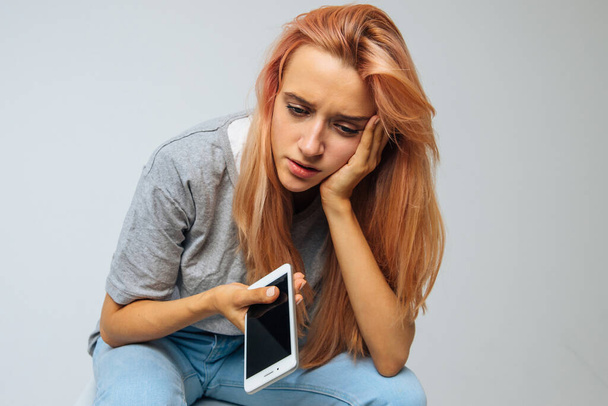 Плачущая одинокая женщина в депрессии смотрит вниз, держит смартфон, получает плохие новости и трогает свою голову. Проблема в отношениях, разрыв отношений, депрессия любви, концепция одиночества - Фото, изображение