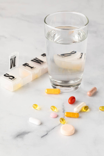 Un primer plano de vitaminas y suplementos dispersos con un vaso de agua y un recipiente de vitaminas. - Foto, Imagen