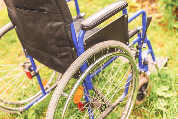 Pusty wózek inwalidzki stojący na trawie w parku szpitalnym, czekający na usługi dla pacjentów. Nieprawidłowy fotel dla osób niepełnosprawnych zaparkowany na zewnątrz w przyrodzie. Dostępny dla niepełnosprawnych symbol. Koncepcja medyczna opieki zdrowotnej - Zdjęcie, obraz