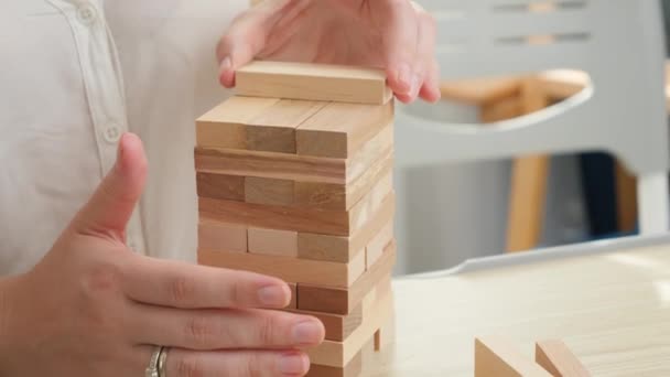Primer plano de la mujer de negocios que construye la torre de bloques de madera y ladrillos. Concepto de estabilidad, desarrollo, éxito y crecimiento empresarial - Metraje, vídeo