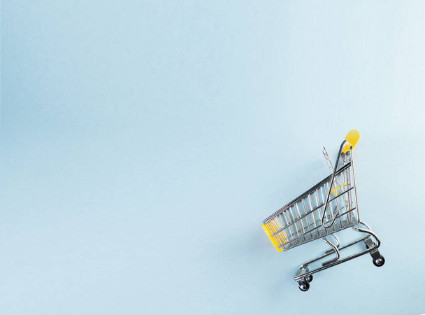 A yellow empty mini shopping cart on pastel blue background. Shopping concept. - Фото, изображение
