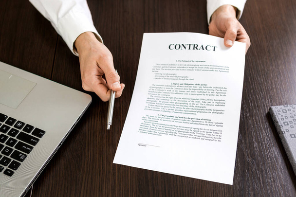 Επιχειρηματίας παραδίδει ένα συμβόλαιο για υπογραφή προσφέροντας ένα ασημένιο στυλό στο χέρι του. - Φωτογραφία, εικόνα