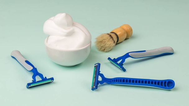 Unas cuantas cuchillas desechables, un cepillo y un tazón de espuma de afeitar. Set para el cuidado de la cara de un hombre. - Foto, Imagen