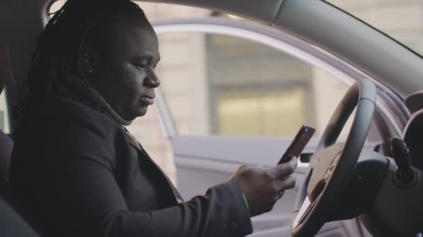 Exitoso hombre afroamericano sorprendido mensaje de texto mientras está sentado en el asiento de los conductores de su coche - Imágenes, Vídeo
