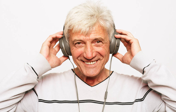 lifestyle, tehnology and old people concept: Senior man listening to music with headphones over white background - Fotó, kép