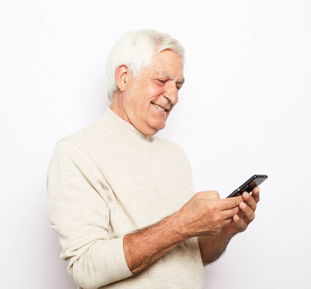Tehnology and old people concept: Portrait of senior man who is messaging on smartphone over white background, close up - Foto, Bild