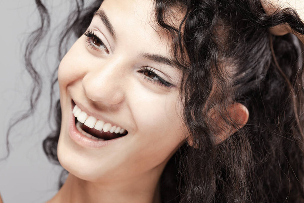 Beautiful brunette girl with long curly hair, studio portrait. Smiling face expression. - Fotó, kép