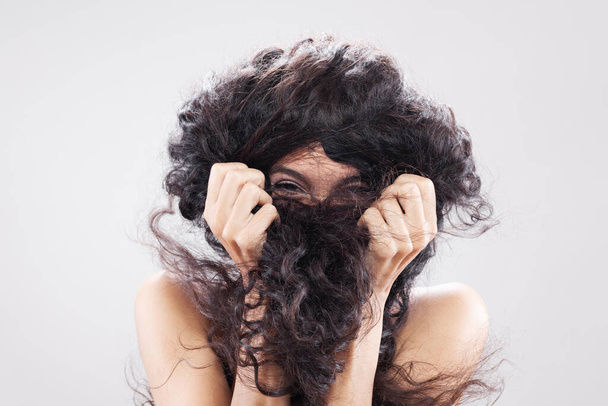 Beautiful brunette girl with long curly hair, studio portrait. Hiding behind the hair. - Fotoğraf, Görsel