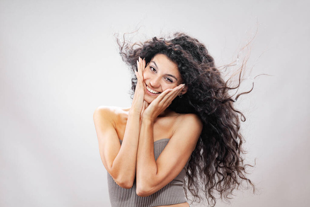 Beautiful brunette girl with long curly hair in the air, studio portrait. Happy smiling face expression. - Fotó, kép