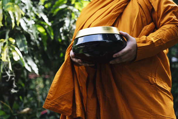 Monge em roupão amarelo segurando uma tigela para a oferta de esmolas pela manhã. - Foto, Imagem