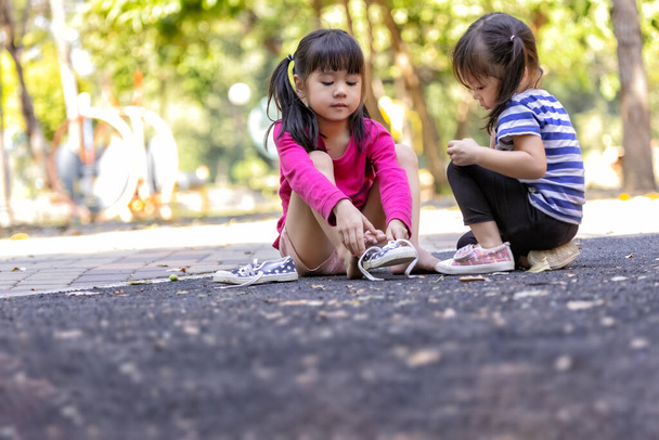 Δύο παιδιά προσπαθούν να φορέσουν παπούτσια μόνα τους στην παιδική χαρά του πάρκου. - Φωτογραφία, εικόνα
