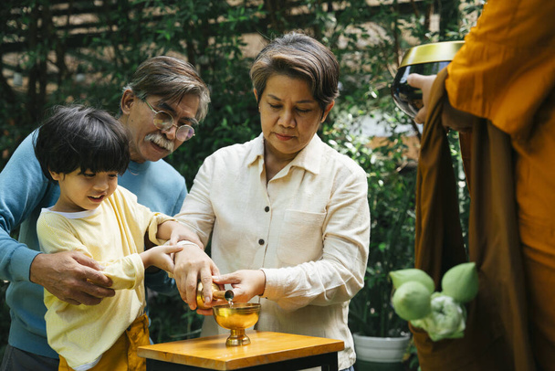 Famiglia asiatica versando acqua dal graal d'oro dopo aver dato elemosina offerta al monaco. - Foto, immagini