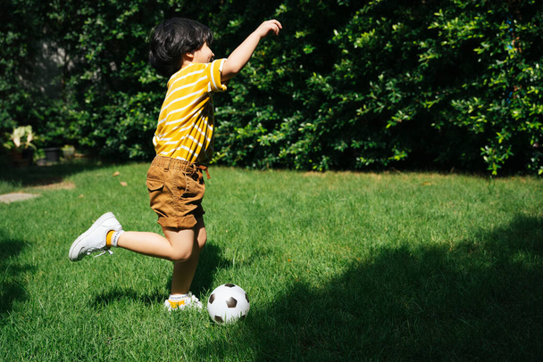 Ноги азиатского мальчика бегают и стреляют с футболом в зеленом поле в парке. - Фото, изображение