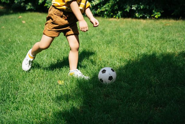 nogi Azji chłopiec działa i strzelanie z piłką nożną w zielony pole w park. - Zdjęcie, obraz