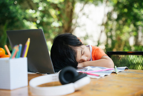 アジアの子供は勉強に疲れたコンピュータのラップトップの前で眠る. - 写真・画像
