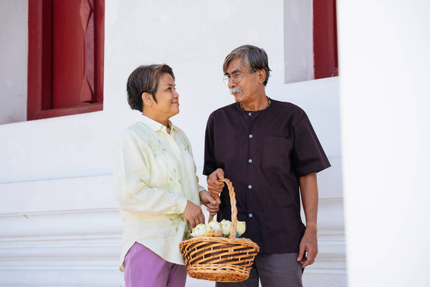 Романтическая азиатская пожилая пожилая пара, держащая корзину с цветами лотоса, делают заслуги в храме. - Фото, изображение