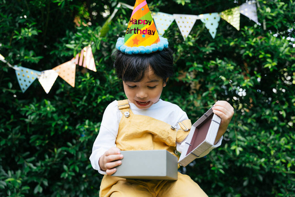 Veselé asijské černošky vlasy dítě nosit klobouk držet dárek box na dvoře. - Fotografie, Obrázek
