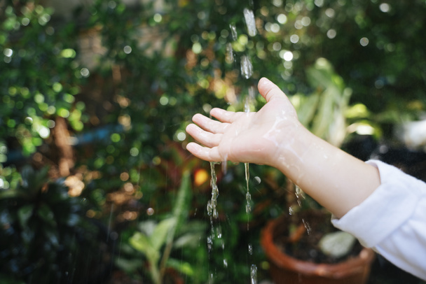 Χέρι του μικρού παιδιού αγγίζει μια σταγόνα βροχής στον κήπο. - Φωτογραφία, εικόνα