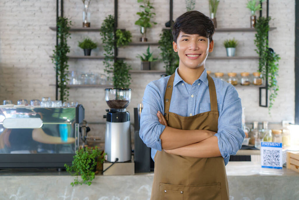 アジアの男バリスタまたは所有者小さいビジネスでエプロン見てカメラと腕交差でザ現代のコーヒーショップ - 写真・画像