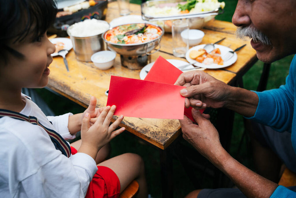 Nagyapa piros borítékot ad a család legfiatalabb tagjának az ebédlőben..  - Fotó, kép