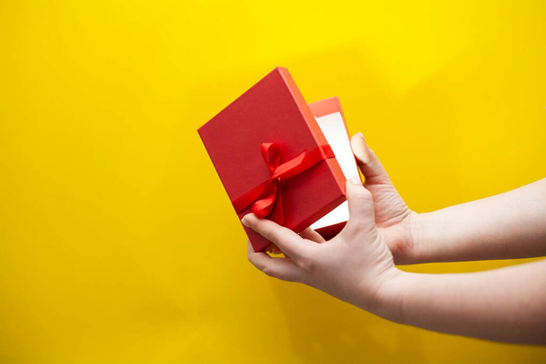 Main de femme tenant boîte cadeau rouge sur fond jaune. Photo de haute qualité. - Photo, image