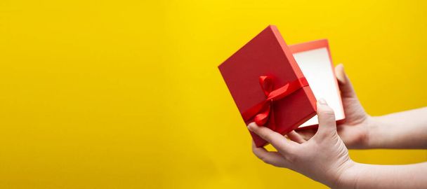 Mano de mujer sosteniendo caja de regalo roja sobre fondo amarillo. Foto de alta calidad. - Foto, imagen