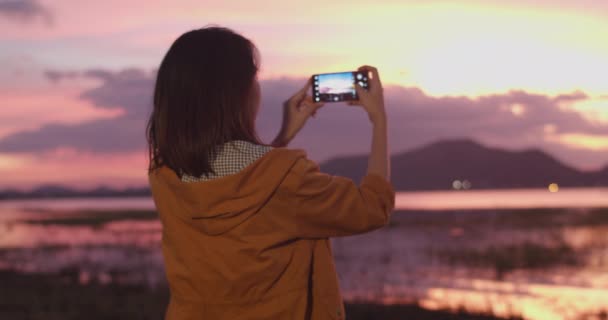 Cheerful young traveler Asian lady with backpack using phone for take a picture in camping on beach at night. Girl enjoy holidays adventure feeling happy freedom. Lifestyle travel and relax concept. - Footage, Video