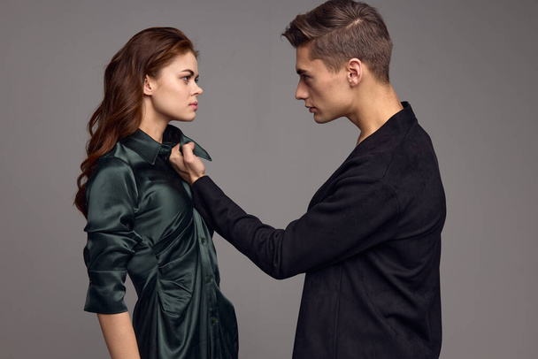 Agressieve man in een pak houdt een vrouw door de kraag van een jurk op een grijze achtergrond - Foto, afbeelding